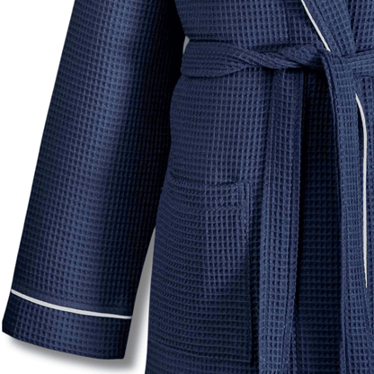 A close-up of a navy blue waffle-weave bathrobe with white piping trim on the cuffs and waist tie, shown against a plain white background.