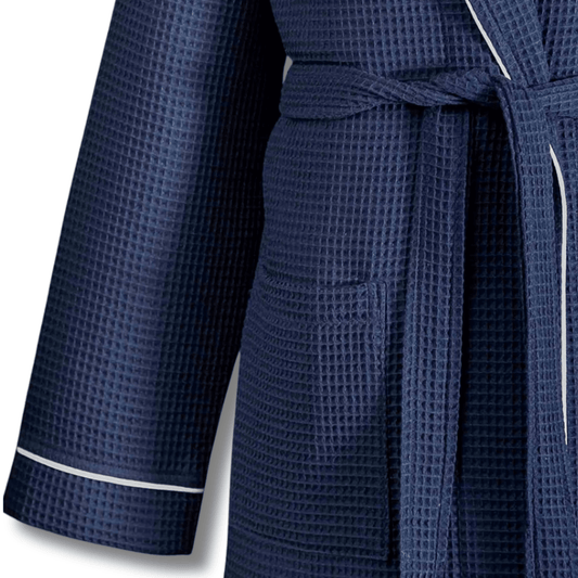 A close-up of a navy blue waffle-weave bathrobe with white piping trim on the cuffs and waist tie, shown against a plain white background.